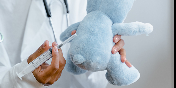 Picture of a blue teddy bear being injected by a white-coated doctor